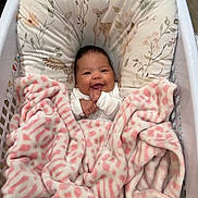 Zara is registered to the contest to win money with this photo: baby, blanket, child, comfort, cozy, cushion, cute, face, floral_pattern, happy, indoor, infant, laundry_basket, person, pink, portrait, resting, smiling, soft, white