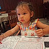 child, toddler, girl, portrait, restaurant, table, coloring, crayon, placemat, drawing, seated, dress, smiling, indoors, chairs, dining_area, checkerboard, food_service, brown_hair, focused