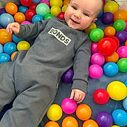 Myles is registered to the contest to win money with this photo: baby, child, smiling, play, ball_pit, colorful, toys, onesie, happy, indoor, face, hand, person, cute, infant, plastic_balls, fun, playtime, bright_colors, joyful