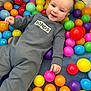 baby, child, smiling, play, ball_pit, colorful, toys, onesie, happy, indoor, face, hand, person, cute, infant, plastic_balls, fun, playtime, bright_colors, joyful