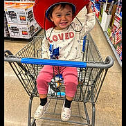 Adaline joined the competition — help win amazing prizes! toddler, child, shopping_cart, red_hat, cowboy_hat, store, aisle, clothing, smiling, playful, footwear, person, retail, indoor, shopping, casual_wear, fun, young_child, hat, happy