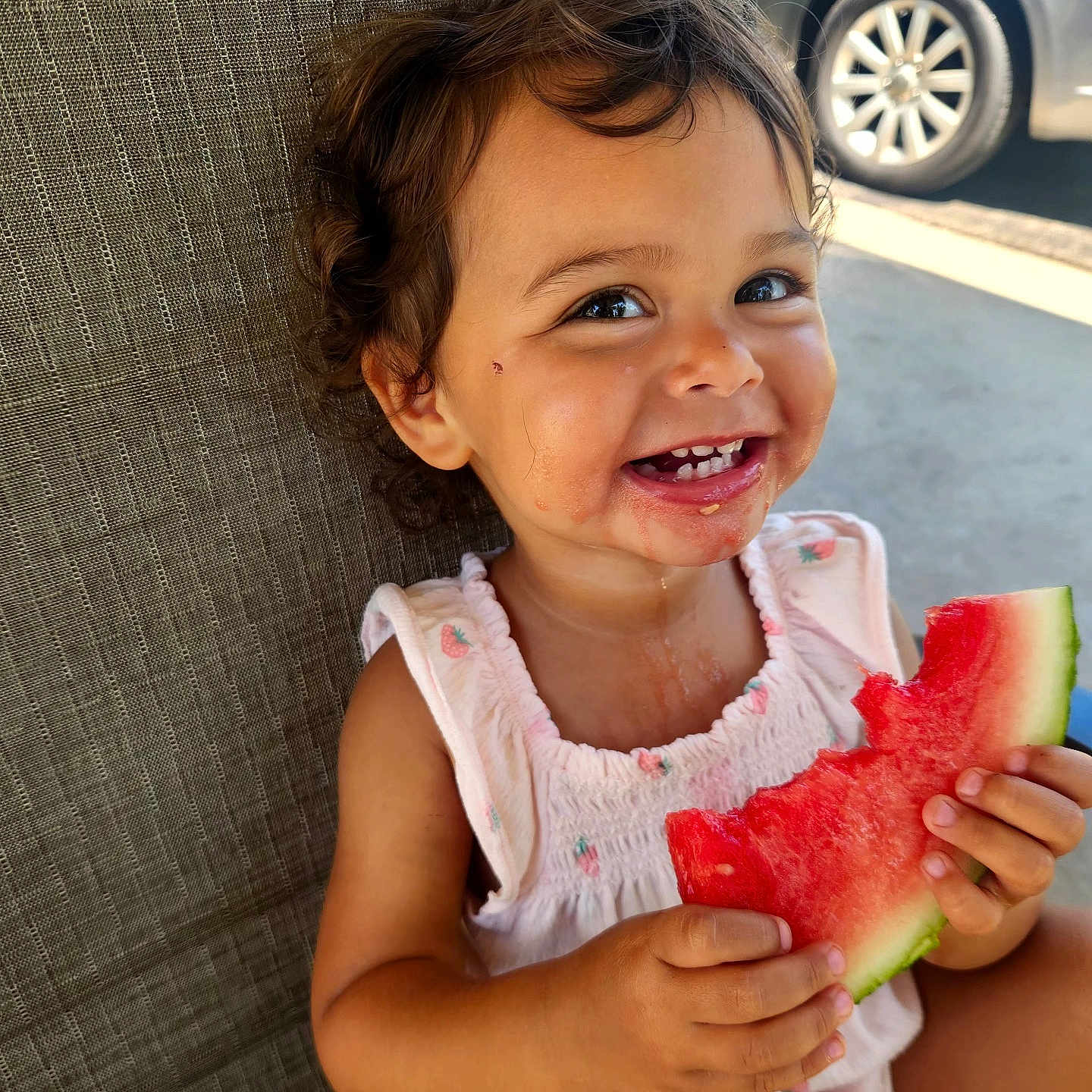 Adaline is registered to the contest to win money with this photo: toddler, child, watermelon, smiling, curly_hair, messy_face, sitting, chair, outdoor, summer, food, fruit, happy, cute, person, clothing, car, background, skin, daylight