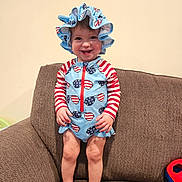 Madelyn joined the competition — help win amazing prizes! child, toddler, smile, hat, sunhat, swimsuit, american_flag_pattern, stripes, stars, red_white_blue, couch, sofa, living_room, bare_feet, standing, hands, face, portrait, toy, upholstery