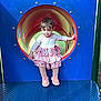 Madelyn is registered to the contest to win money with this photo: child, toddler, playground, tunnel, slide, dress, frills, striped_leggings, sneakers, shoes, blue_panel, metal_platform, grass, outdoor, curious_expression, standing, portrait, play_equipment, colorful, young_kid