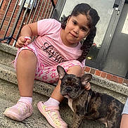 Goofy is registered to the contest to win money with this photo: child, dog, puppy, stairs, brick_wall, concrete, outdoor, building, girl, pet, animal, cute, casual_clothing, pajamas, slippers, curly_hair, braid, metal_railing, door, daylight