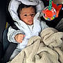 Omar participe au concours pour gagner de l'argent avec cette photo : baby, infant, car_seat, blanket, onesie, hooded_clothing, toy, plush, face, child, cute, warm, indoor, portrait, expression, small_hand, fabric, colorful, seatbelt, comfort