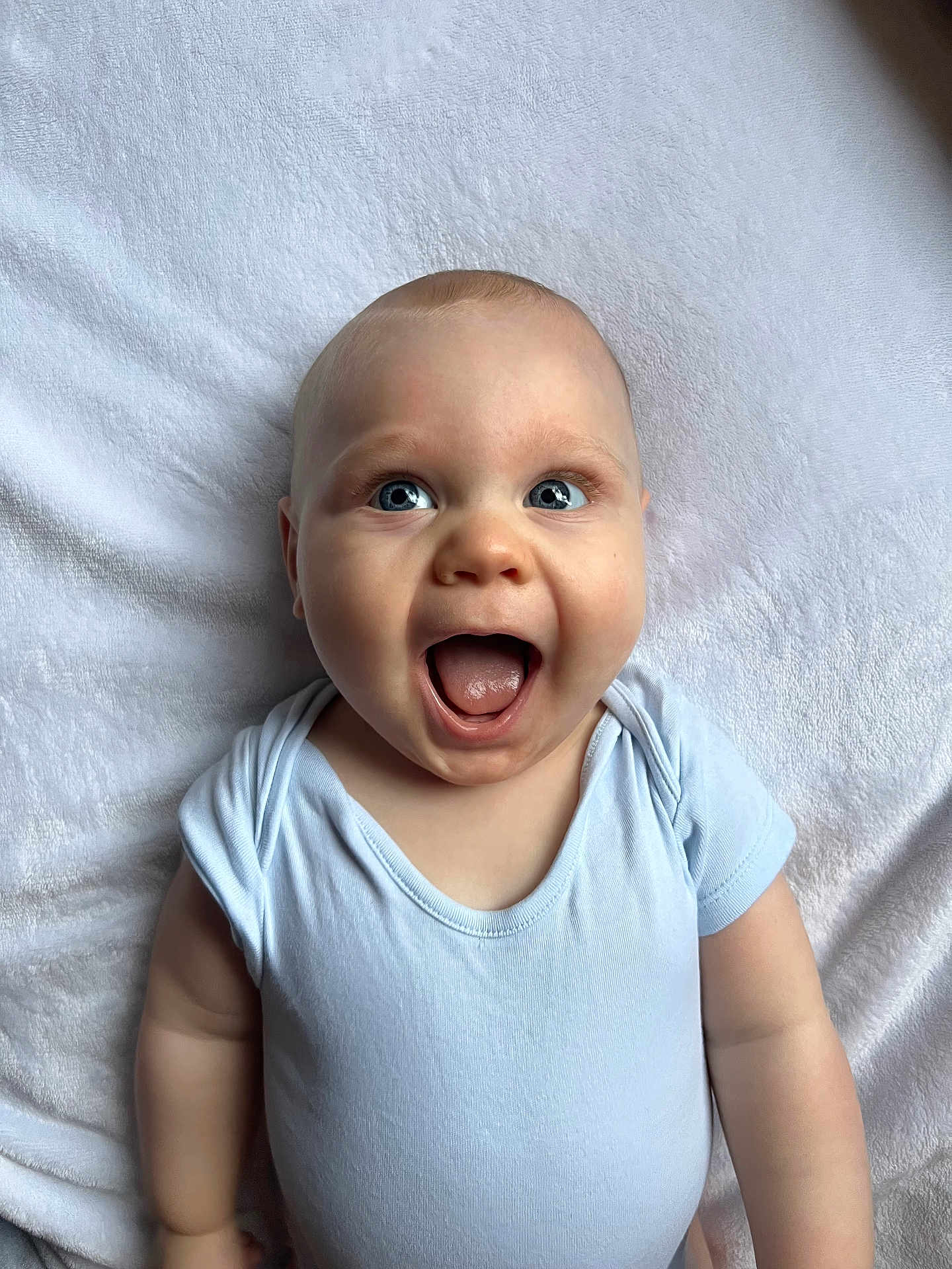 Jaxon joined the competition — help win amazing prizes! baby, infant, blue_eyes, onesie, smiling, happy, lying_down, blanket, soft_texture, cute, human, child, portrait, skin, head, mouth_open, small_hands, cheeks, expression, indoors