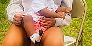 Charvis Jr joined the competition — help win amazing prizes! toddler, child, adult, sitting, outdoor, grass, chair, white_shirt, red_shorts, socks, folding_chair, holding, person, casual_clothing, greenery, daylight, brick_wall, curly_hair, relaxed, family