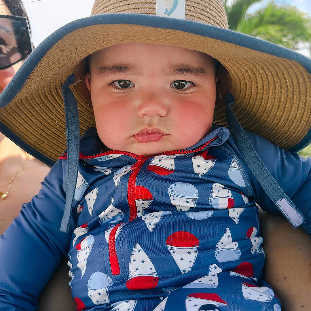 Jett joined the competition — help win amazing prizes! baby, child, sunhat, blue_outfit, patterned_clothing, face, outdoor, sky, greenery, person, hand, adult, holding, summer, cute, portrait, expression, sunny, day, casual