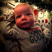 Riley joined the competition — help win amazing prizes! baby, infant, mittens, holiday, christmas, blanket, lights, greenery, clothing, face, portrait, cute, indoors, festive, expression, lying_down, warm_lighting, soft_texture, red, gray