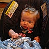 Kordova joined the competition — help win amazing prizes! baby, child, blanket, car_seat, blue_blanket, warning_label, indoors, cute, person, young_child, infant, hair_tie, black_shirt, expression, seated, face, small_hands, cozy, home, portrait