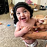 Kaiya is registered to the contest to win money with this photo: baby, child, smiling, diaper, black_bonnet, tattoo, arm, dog, carpet, indoor, person, happy, cute, holding, room, box, toy, footwear, furniture, playful