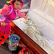 Roseary is registered to the contest to win money with this photo: child, costume, pink, skeleton, coffin, halloween, candy, bucket, spider_web, outdoor, daylight, trick_or_treat, toy, face, person, holiday, celebration, event, fun, playful