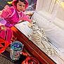 child, costume, pink, skeleton, coffin, halloween, candy, bucket, spider_web, outdoor, daylight, trick_or_treat, toy, face, person, holiday, celebration, event, fun, playful