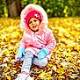 Roseary is registered to the contest to win money with this photo: child, toddler, autumn, leaves, pink_jacket, mittens, beanie, outdoor, sitting, smiling, nature, forest, fall, seasonal, happy, portrait, casual_wear, footwear, daylight, young