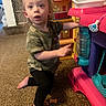 toddler, child, indoor, carpet, toy_kitchen, plastic_toy, curious, kneeling, playtime, expression, camo_shirt, black_pants, barefoot, home, furniture, colorful, young_child, exploration, person, casual_clothing