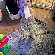 Lilyana is registered to the contest to win money with this photo: toddler, baby, child, indoor, carpet, baby_bottle, spoon, headband, yellow_clothing, barefoot, toy, baby_gate, floor, person, standing, cute, playful, home, carpet_pattern, infant