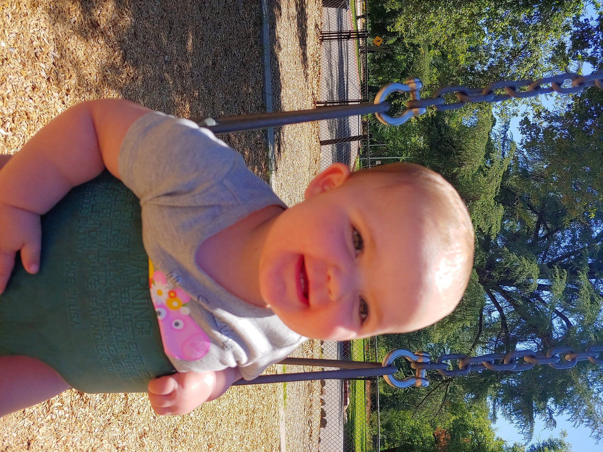 Sydney is registered to the contest to win money with this photo: child, face, fun, grass, happy, human_body, human_leg, joy, leaf, leisure, outdoor_play_equipment, people_in_nature, person, plant, smile, summer, sunlight, t_shirt, toddler, tree
