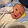 baby, newborn, infant, face, eyes, mouth, onesie, clothing, blanket, blue_blanket, yellow_pattern, white_clothing, cute, lying_down, soft_texture, small_hand, expression, indoors, portrait, cozy
