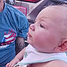 baby, child, face, profile, bib, person, adult, tattoo, blue_shirt, eagle_design, car, vehicle, outdoor, daylight, skin, hand, ear, hair, clothing, closeup