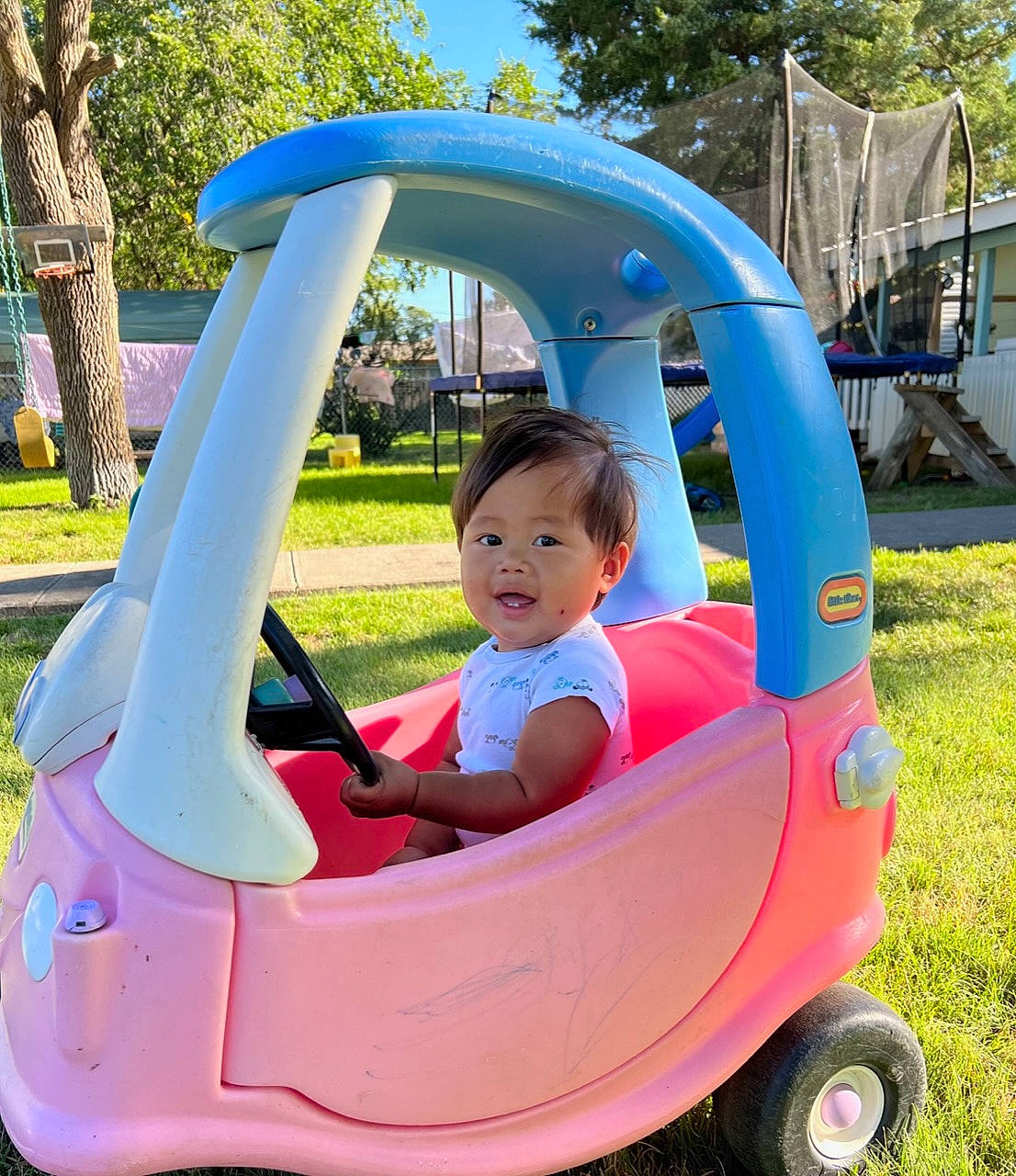 Jordan is registered to the contest to win money with this photo: baby, baby_toddler_clothing, blue, child, comfort, fun, grass, happy, leisure, magenta, motor_vehicle, person, plant, recreation, sitting, summer, tire, toddler, tree, vehicle