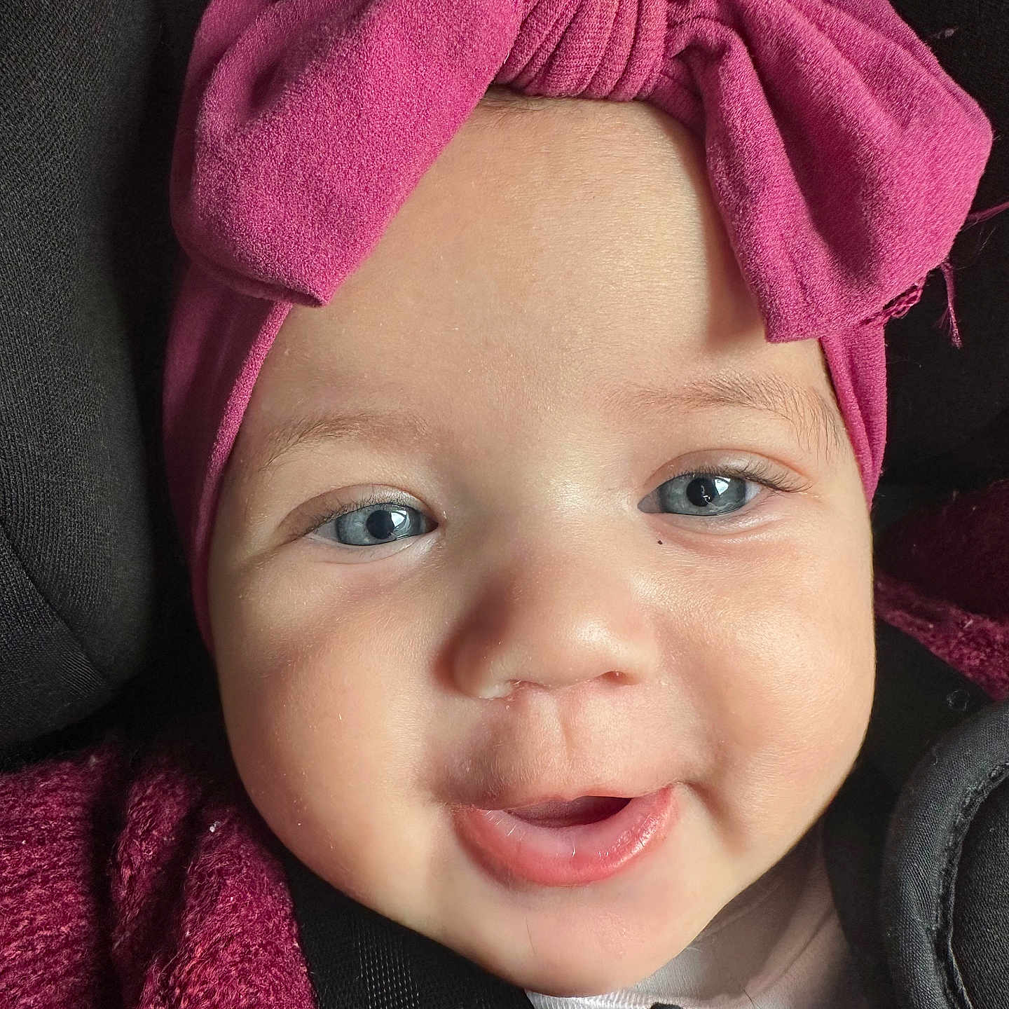 Dahlia is registered to the contest to win money with this photo: baby, blue_eyes, car_seat, child, chubby_cheeks, closeup, clothing, cute, face, happy, headband, headwear, indoors, infant, pink, portrait, seatbelt, smile, sweater, young