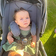 Dahlia joined the competition — help win amazing prizes! baby, stroller, child, green_dress, blue_eyes, sunlight, outdoor, grass, toy, seatbelt, curly_hair, pigtails, infant, sitting, childcare, daylight, playful, portrait, cute, baby_accessory