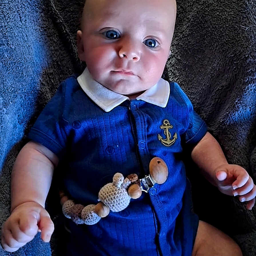 Malo participe au concours pour gagner de l'argent avec cette photo : baby, infant, blue_outfit, pacifier_clip, beads, crochet, wooden_beads, blanket, texture, collar, navy_blue, cute, child, young, sitting, indoors, portrait, person, skin, hand