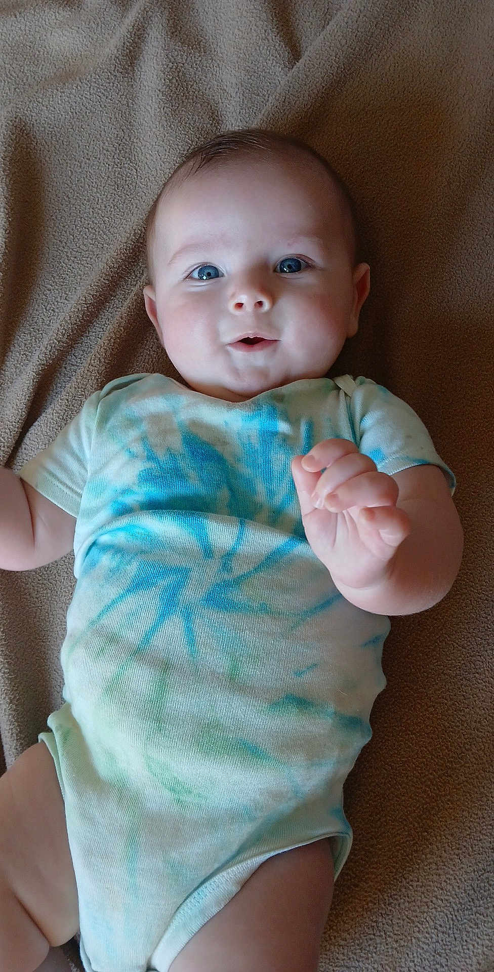 Landry joined the competition — help win amazing prizes! baby, infant, onesie, blue_eyes, tie_dye, blanket, soft_texture, cute, lying_down, hand, skin, cheeks, child, happy, portrait, indoor, apparel, person, newborn, smiling