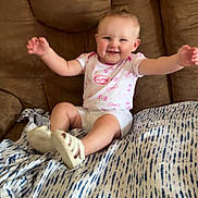 Wrenlee is registered to the contest to win money with this photo: baby, child, smiling, sitting, couch, blanket, indoor, happy, person, footwear, white_clothing, pink_pattern, face, arms, legs, soft_shoes, home, comfort, infant, cute
