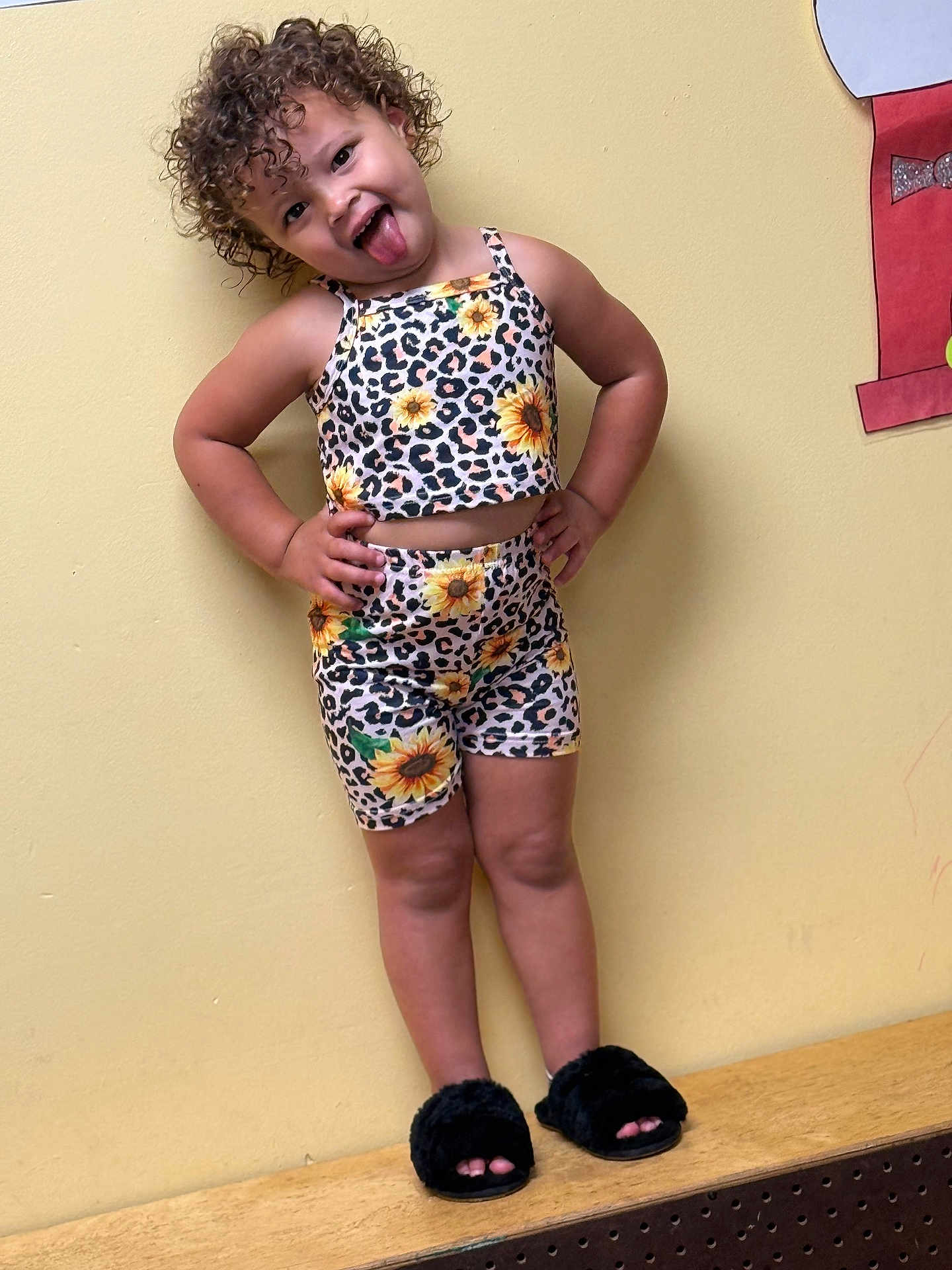 Oaklynn is registered to the contest to win money with this photo: child, curly_hair, tongue_out, yellow_wall, sunflower_print, leopard_print, matching_outfit, shorts, tank_top, black_slippers, standing, playful, indoor, smiling, cute, pose, person, fashion, happy, cheeky