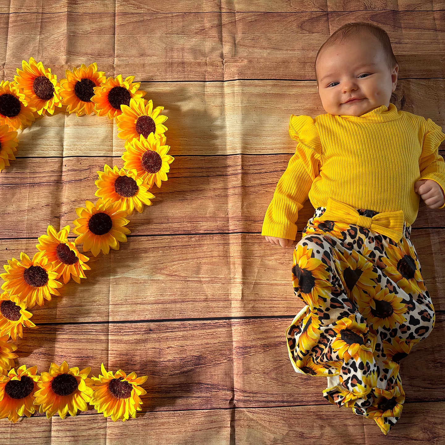 Victoire a rejoint le concours — aidez-le/la à gagner de superbes lots ! adorable, baby, baby_fashion, bright_colors, child, cute, dimples, floral_pattern, happy, indoors, infant, lying_down, number_two, patterned_pants, playful, portrait, smiling, sunflowers, wooden_floor, yellow_clothing