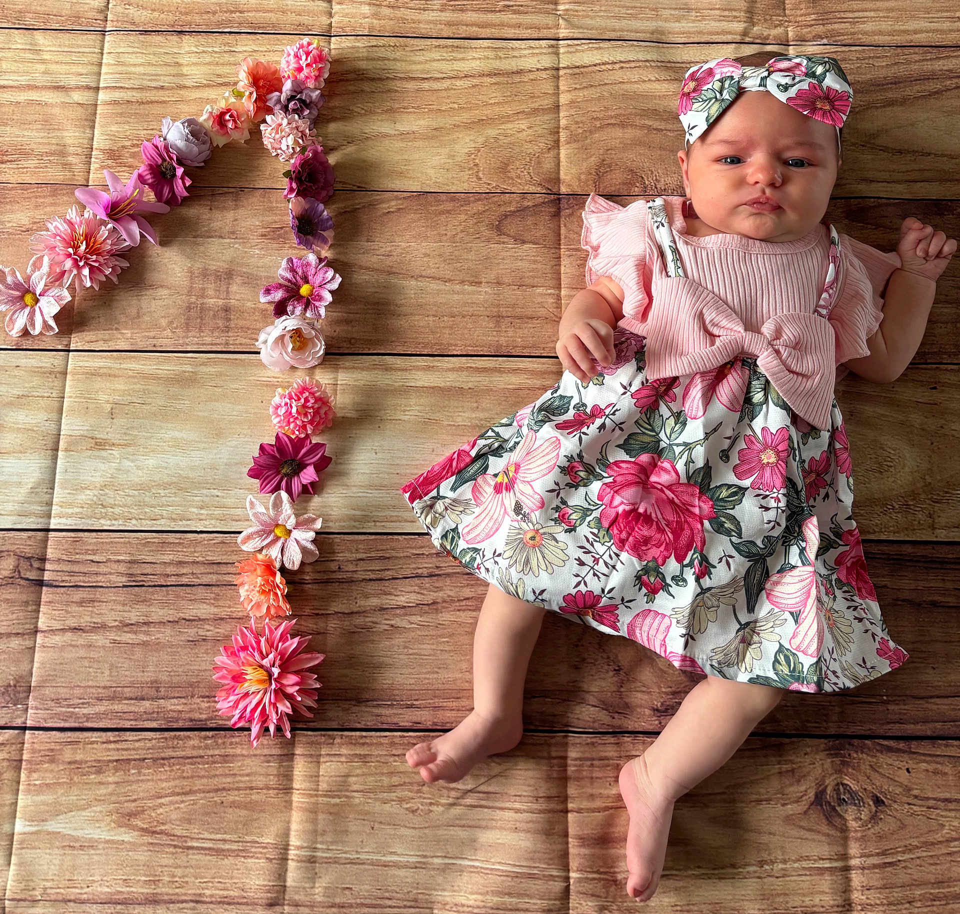 Victoire participe au concours pour gagner de l'argent avec cette photo : baby, infant, flower, headband, dress, floral_pattern, number_one, wooden_floor, flooring, celebration, birthday, cute, child, laying_down, pink, decor, fabric, person, young_child, portrait