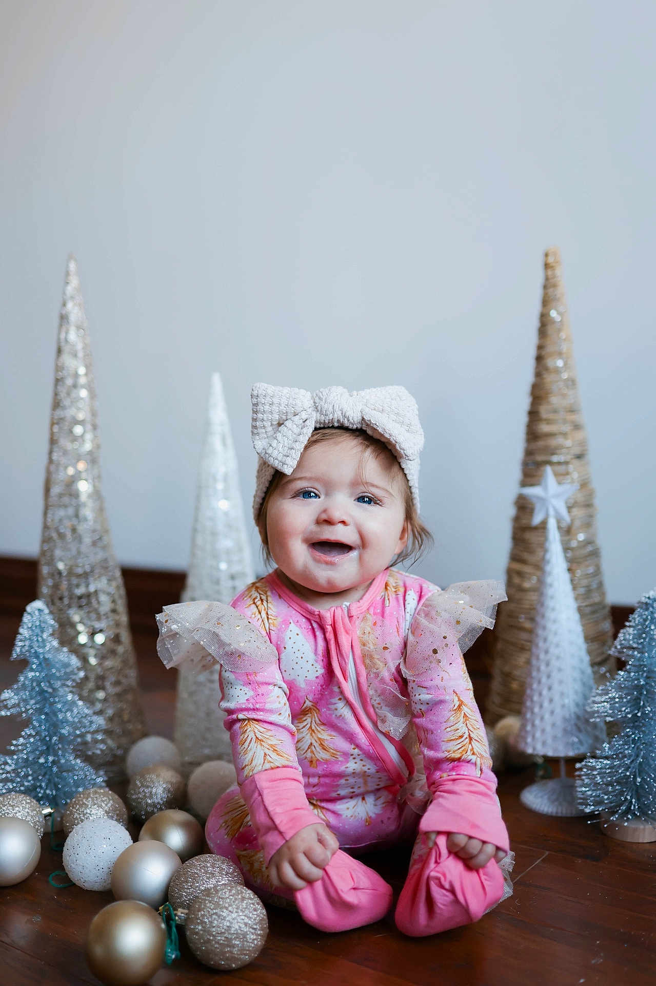 Auburn is registered to the contest to win money with this photo: baby, child, smiling, headband, bow, pink_clothing, christmas, holiday_decor, ornaments, decorative_trees, floor, indoor, happy, cute, sitting, festive, celebration, portrait, infant, winter