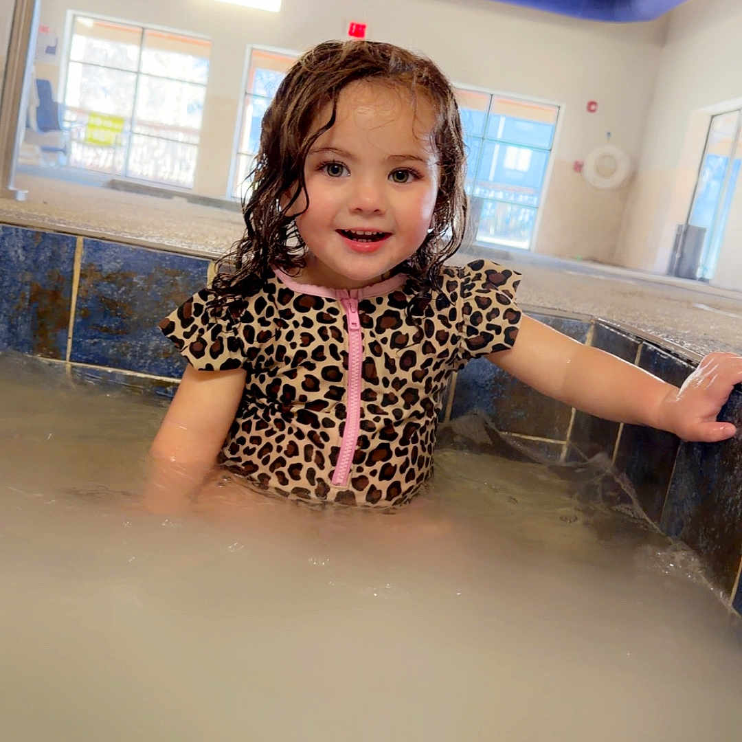 Kaylee joined the competition — help win amazing prizes! child, smiling, swimsuit, leopard_print, wet_hair, indoor_pool, water, splashing, edge, holding, happy, portrait, young_child, playful, bright, natural_light, windows, ceiling, room, fun