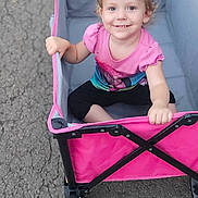 Eleanore is registered to the contest to win money with this photo: toddler, child, wagon, pink_shirt, smiling, outdoor, asphalt, toy, play, happy, sitting, blond_hair, casual_clothing, daylight, small_cart, grip, cute, young_child, portrait, fun