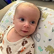 Zayden joined the competition — help win amazing prizes! baby, infant, child, face, eyes, clothing, onesie, football_pattern, blanket, dinosaur_pattern, lying_down, smile, skin, hair, close_up, indoor, soft_light, cute, portrait, young