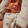 baby, sleeping, onesie, heart_pattern, headband, bow, infant, closeup, face, peaceful, cute, child, soft_lighting, hand, skin, portrait, indoors, newborn, clothing, resting