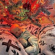Haven is registered to the contest to win money with this photo: baby, newborn, sleeping, blanket, pajamas, christmas_tree, ornaments, lights, snowman_decoration, holiday, indoor, cozy, festive, cross, flower_pattern, soft_texture, decor, celebration, resting, infant