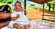 Coreyanna joined the competition — help win amazing prizes! baby, child, infant, dress, bonnet, blanket, outdoor, pavilion, person, skin, hand, footwear, sitting, support, nature, greenery, table, bench, sunlight, candid