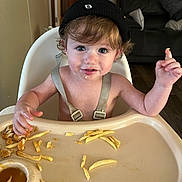 Braxton is registered to the contest to win money with this photo: child, toddler, highchair, fries, snack, food, beanie, hat, messy, smile, face, eyes, hands, tray, dining, living_room, sofa, floor, person_in_background, meal