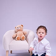 Gael joined the competition — help win amazing prizes! child, toddler, baby, portrait, kneeling, sitting, teddy_bear, armchair, indoors, studio, white_shirt, blue_pants, curly_hair, curious, expression, toy, furniture, pastel_background, photography, family