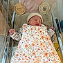 baby, bassinet, bed, birth_details, blanket, clothing, cute, floral_pattern, hat, hospital, indoor, infant, newborn, peaceful, person, pink_pillow, resting, sleeping, soft_texture, wooden_plaques