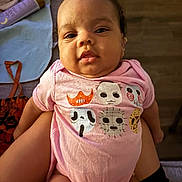 Shai is registered to the contest to win money with this photo: baby, infant, child, onesie, pink_clothing, face, expression, indoor, lap, person, skin, short_sleeves, human, cute, young_child, sitting, soft_lighting, closeup, comfort, casual