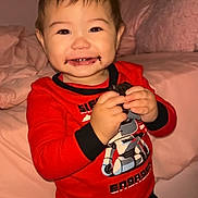 Adonis is registered to the contest to win money with this photo: toddler, child, smiling, chocolate, cookie, pajamas, red_shirt, robot_design, bedroom, bed, blanket, pink, happy, indoor, person, cute, hair_up, holding, standing, face