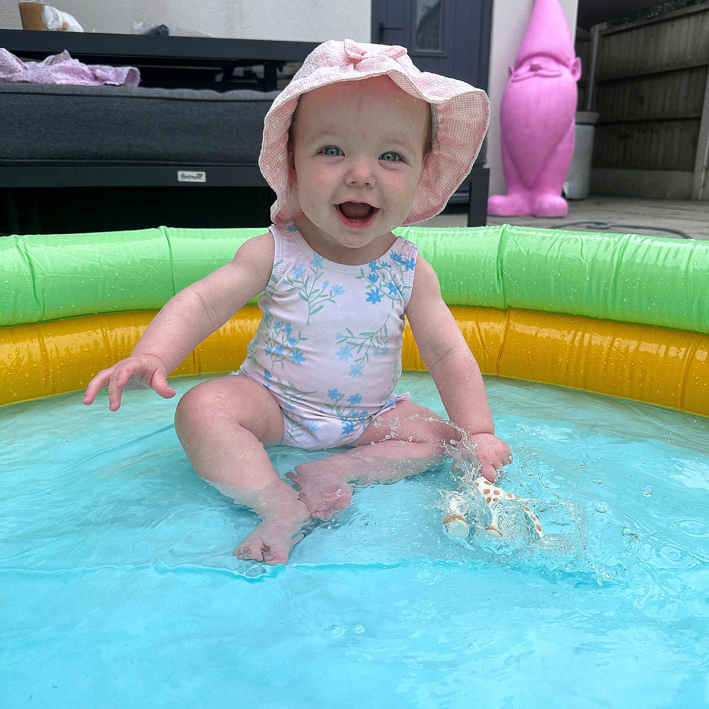 Elsie is registered to the contest to win money with this photo: baby, backyard, blue_water, child, cute, fun, garden_gnome, happy, inflatable_pool, outdoor, pink_hat, play, pool, sitting, smiling, splashing, summer, swimsuit, toy, water
