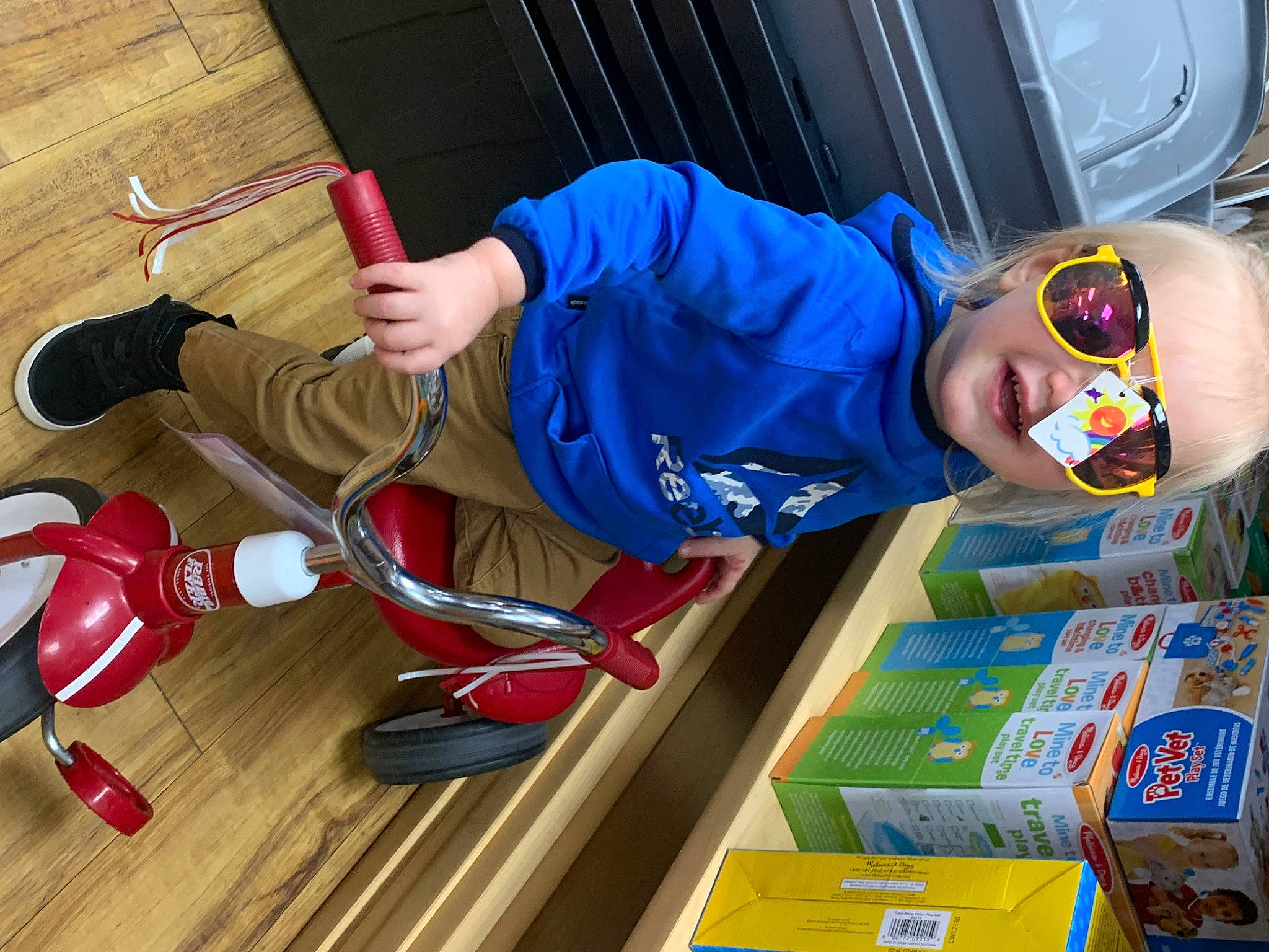 Greyson is registered to the contest to win money with this photo: bicycle_handlebar, chair, child, electric_blue, eyewear, flooring, fun, person, personal_protective_equipment, play, sandal, sportswear, toddler, toy, under_exposed, vehicle, vehicle_door