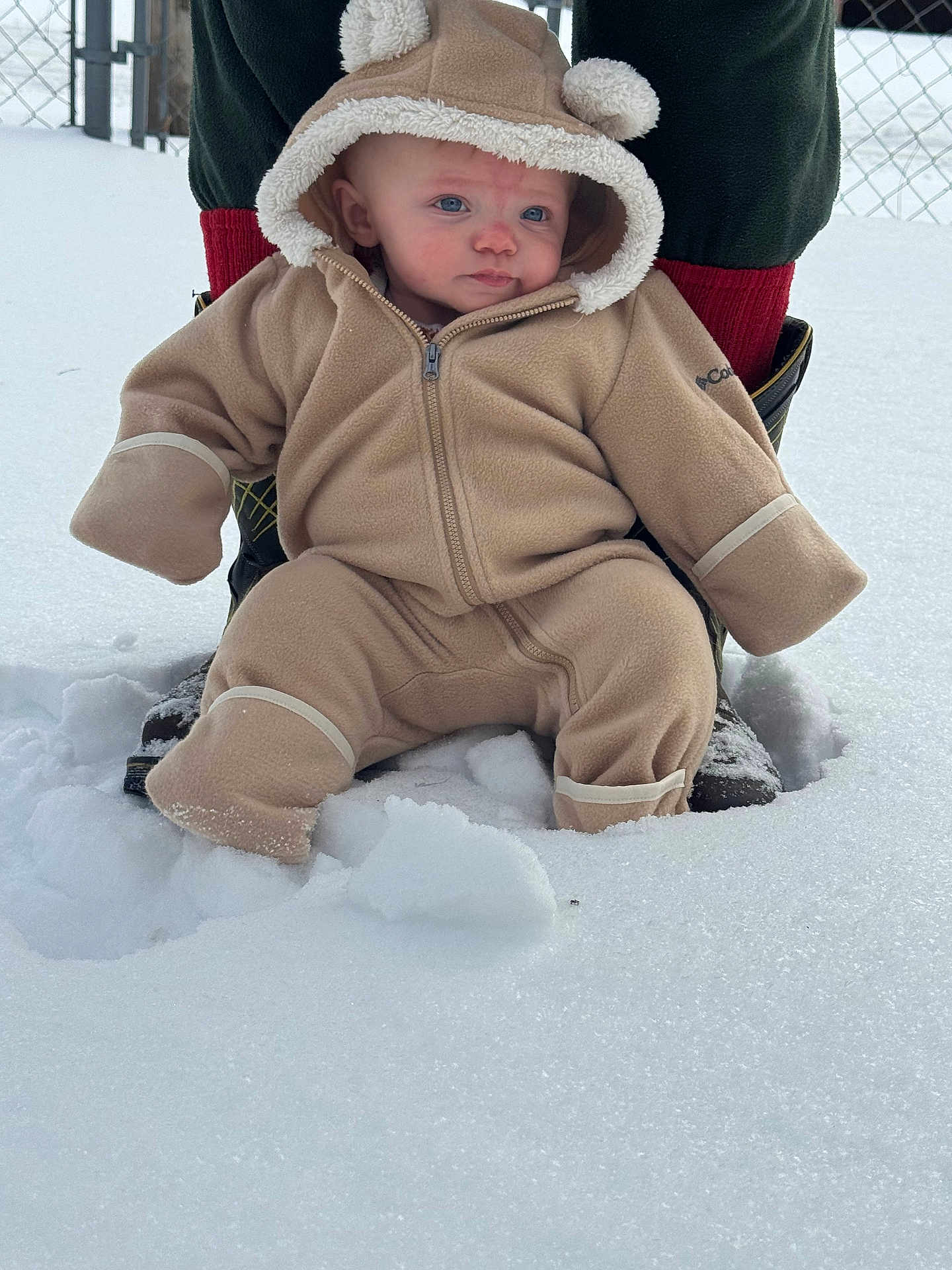 Alexander joined the competition — help win amazing prizes! baby, child, snow, winter_clothing, snowsuit, hood, blue_eyes, outdoor, cold_weather, adult_support, boots, fence, curious_expression, warm_clothing, snowy_ground, fleece, cute, person, baby_pose, winter