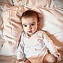 baby, child, infant, bed, pillow, blanket, white_clothing, onesie, looking_at_camera, indoors, soft_lighting, cute, young_child, sitting, face, skin, expression, comfort, rest, cozy