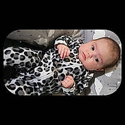 Anna is registered to the contest to win money with this photo: baby, infant, onesie, leopard_print, patterned_clothing, cushion, cloud_pattern, star_pattern, lying_down, curious_expression, indoor, portrait, child, cute, soft_toys, sleepwear, comfortable, young_child, face, small_hands
